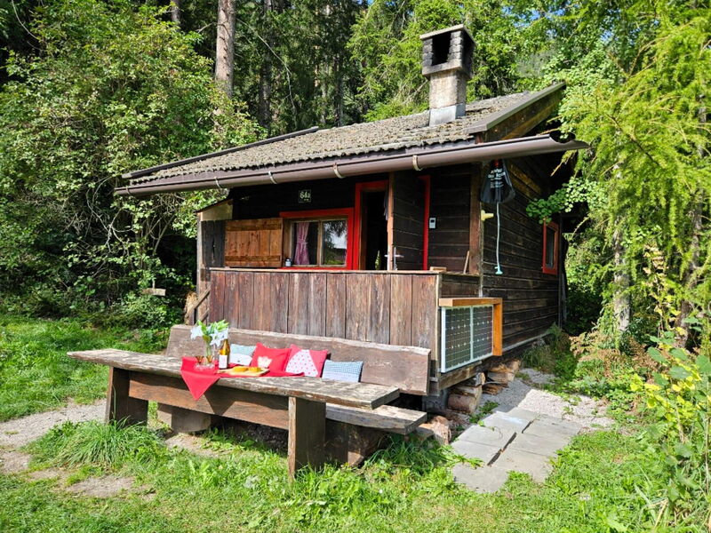 Seitenansicht des Waldhüttls in Terfens mit verwitterter Holzbank vor der Tür und sommerlicher Wiese.