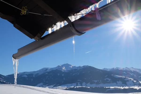 Eiszapfen an der Dachrinne des Waldhüttl, dahinter die verschneiten Berge